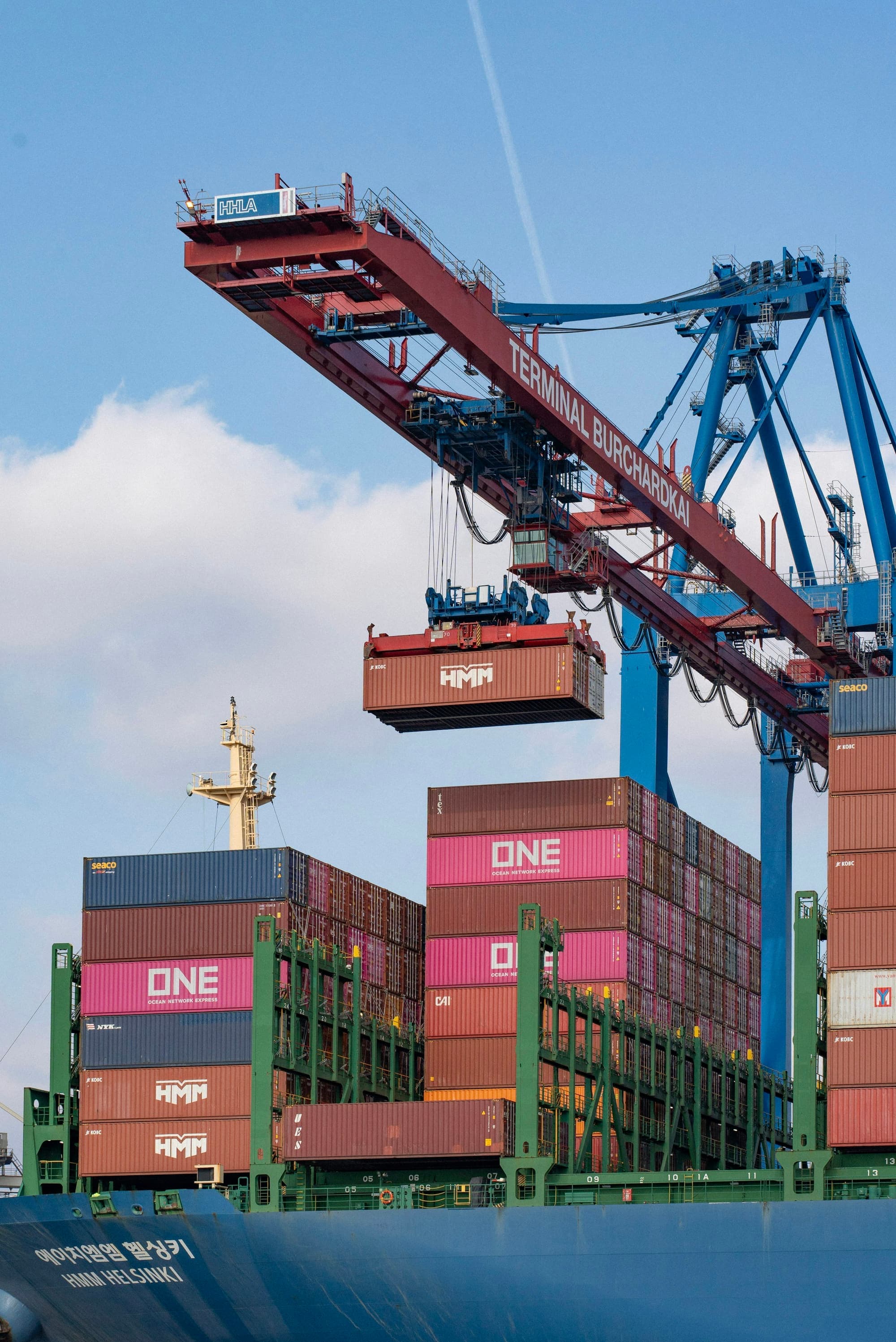 A quayside gantry crane lifting a shipping container above stacked containers
