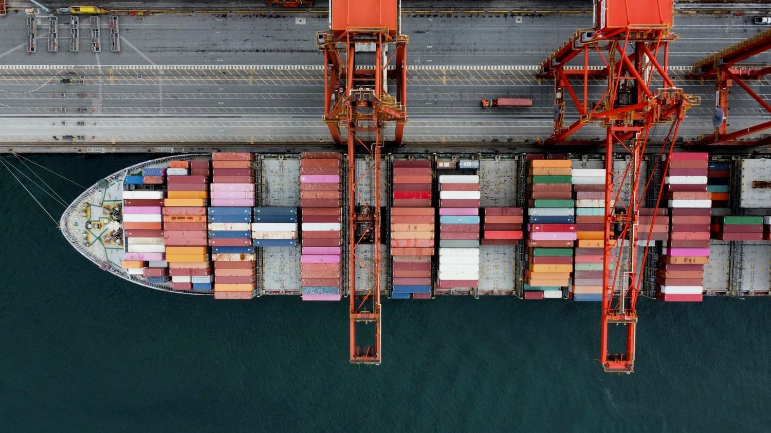 A container ship alongside the quay being worked by gantry cranes, seen from above